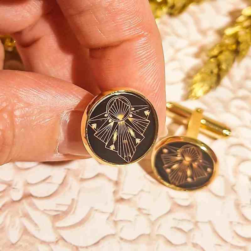 Boutons de Boutons de manchettes dorés faits-main avec motif art déco sur fond noir, présentés sur une surface neutre