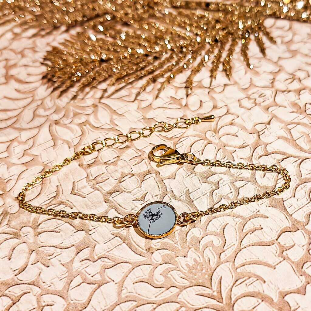 Bracelet minimaliste motif dandelion en laiton doré 24K et acier inoxydable, médaillon rond avec résine brillante, posé sur fond neutre