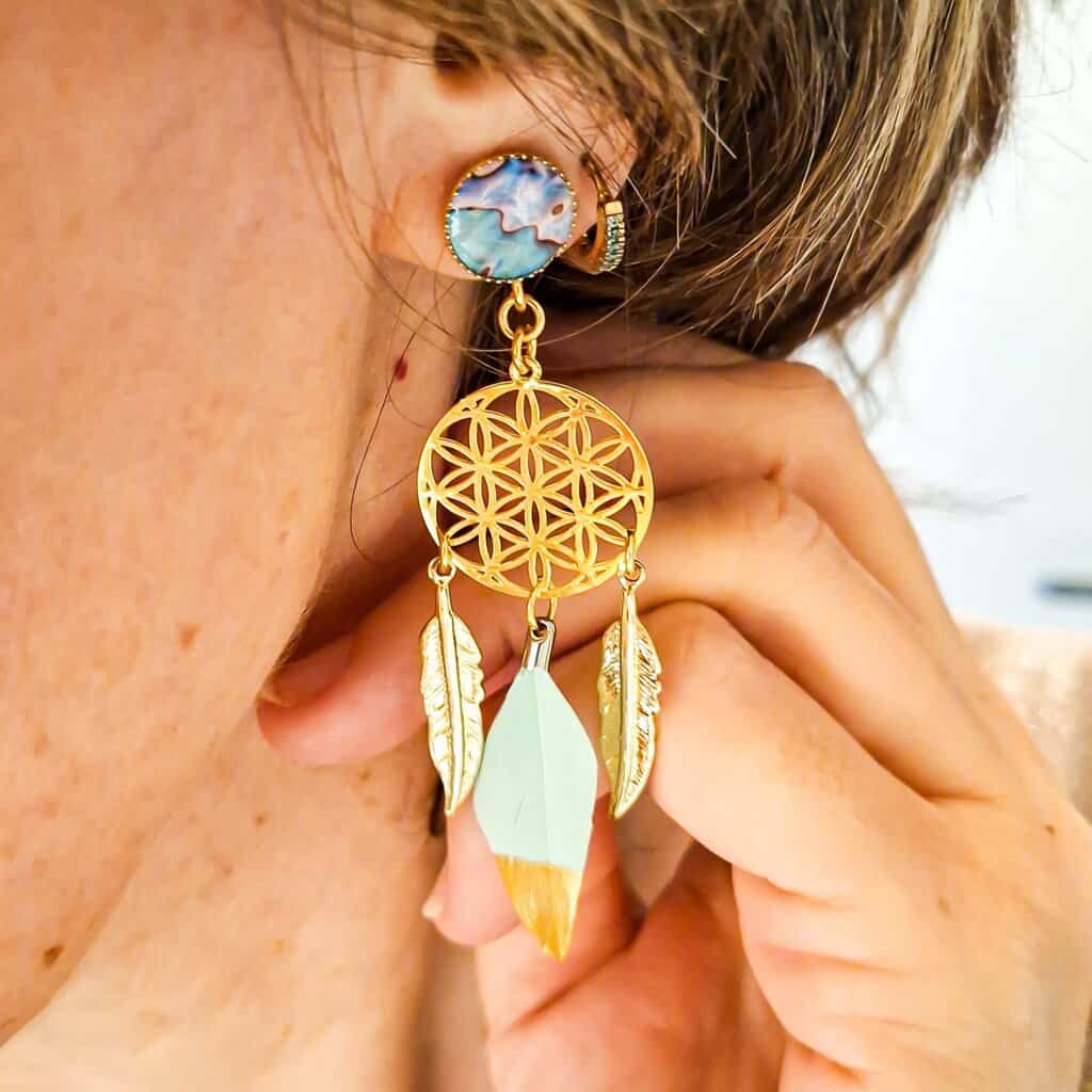 Boucles Fleurs de Vie bohèmes portées, mettant en valeur le motif nacré, les fleurs ajourées et les plumes