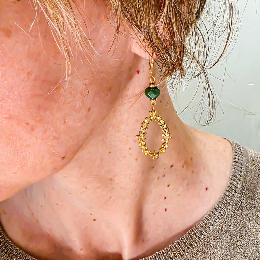 Gros plan sur boucle d’oreille couronne laurier en laiton doré 24k avec perles facettées et heishi, photo portée mettant en valeur les détails et la finesse du pendentif