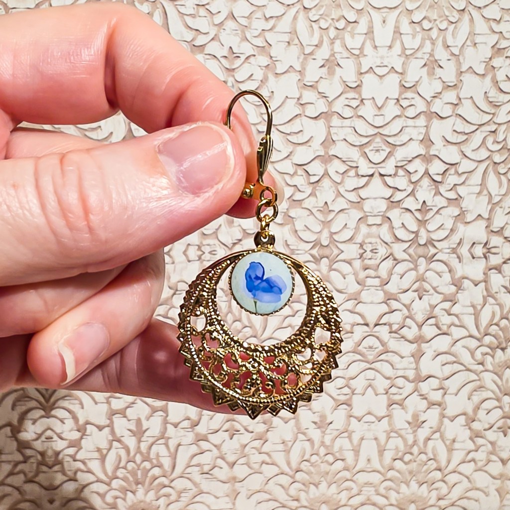 Gros plan sur une boucle d’oreille bleue et dorée avec motif floral en résine, bijou fait-main léger et poétique, style bohème