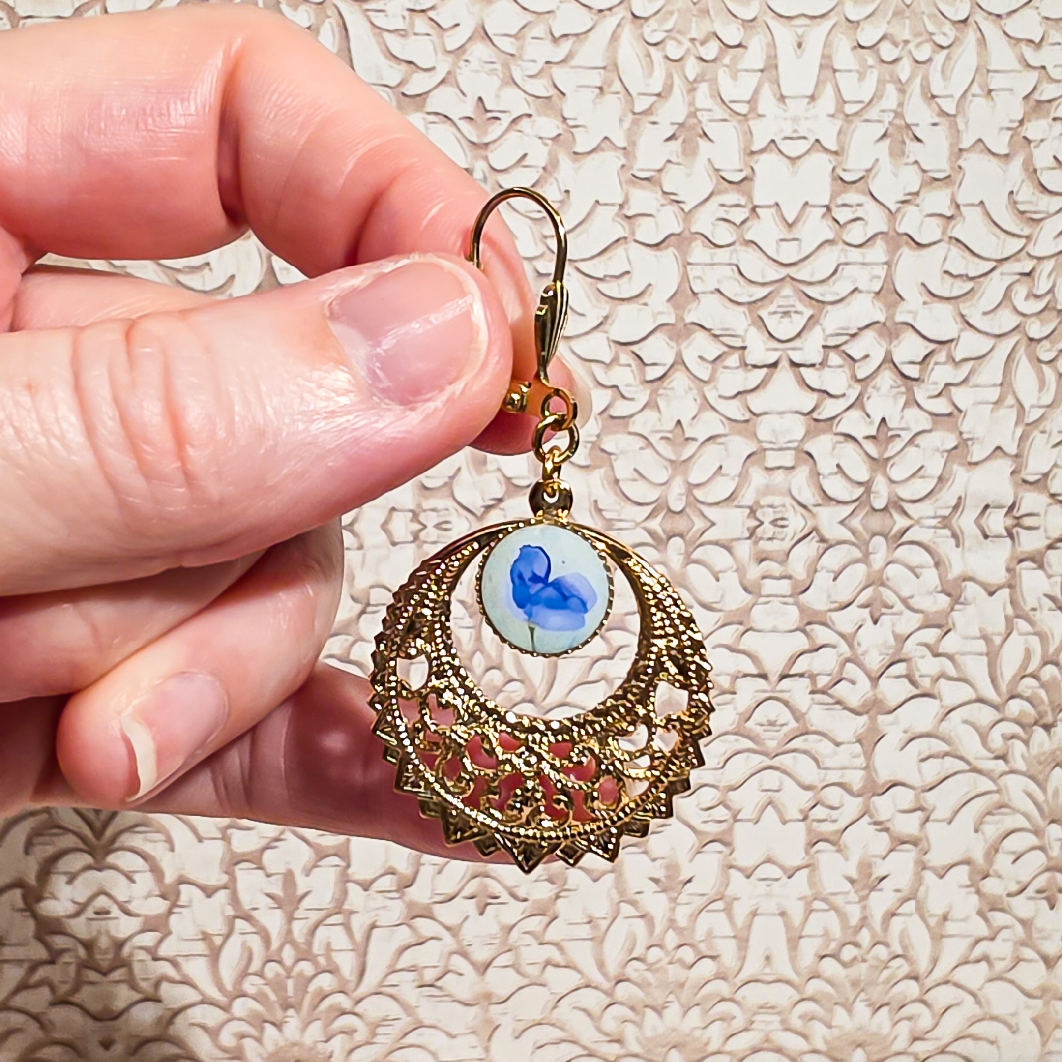 Gros plan sur une boucle d’oreille bleue et dorée avec motif floral en résine, bijou fait-main léger et poétique, style bohème