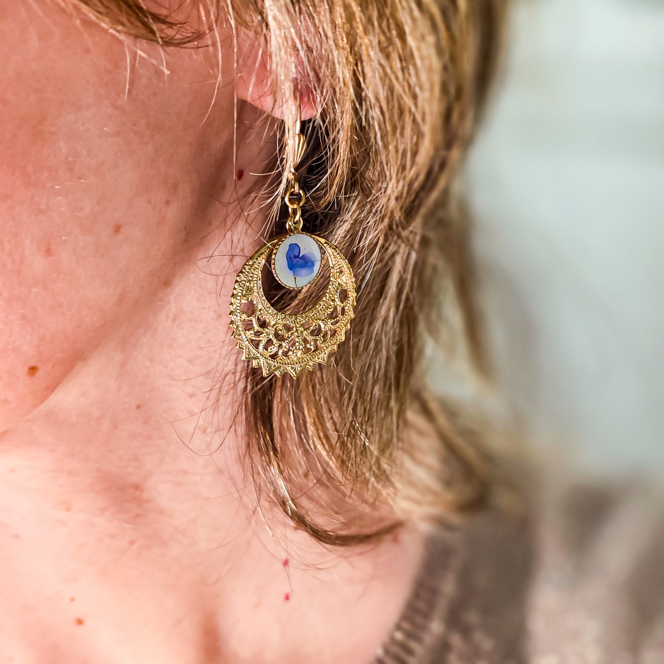 Femme portant des boucles créoles bleues et dorées, bijou bohème chic aux motifs floraux, inspiration végétale et élégance naturelle