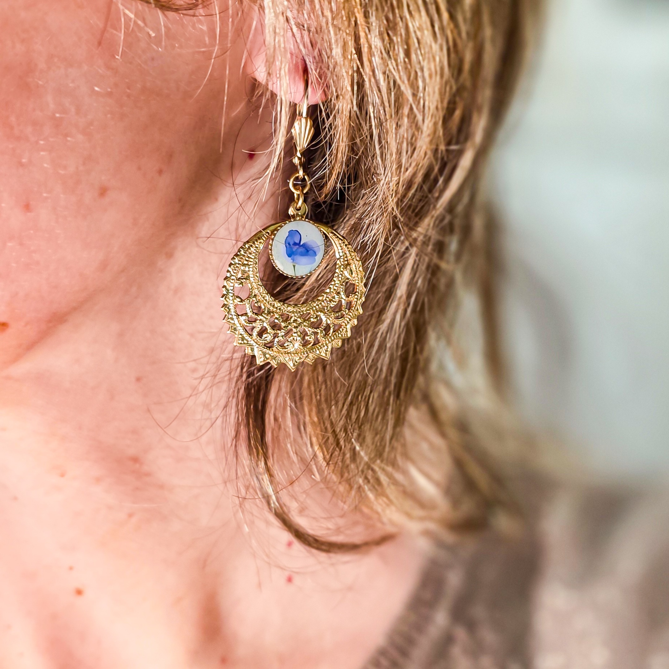 Femme portant des boucles créoles bleues et dorées, bijou bohème chic aux motifs floraux, inspiration végétale et élégance naturelle