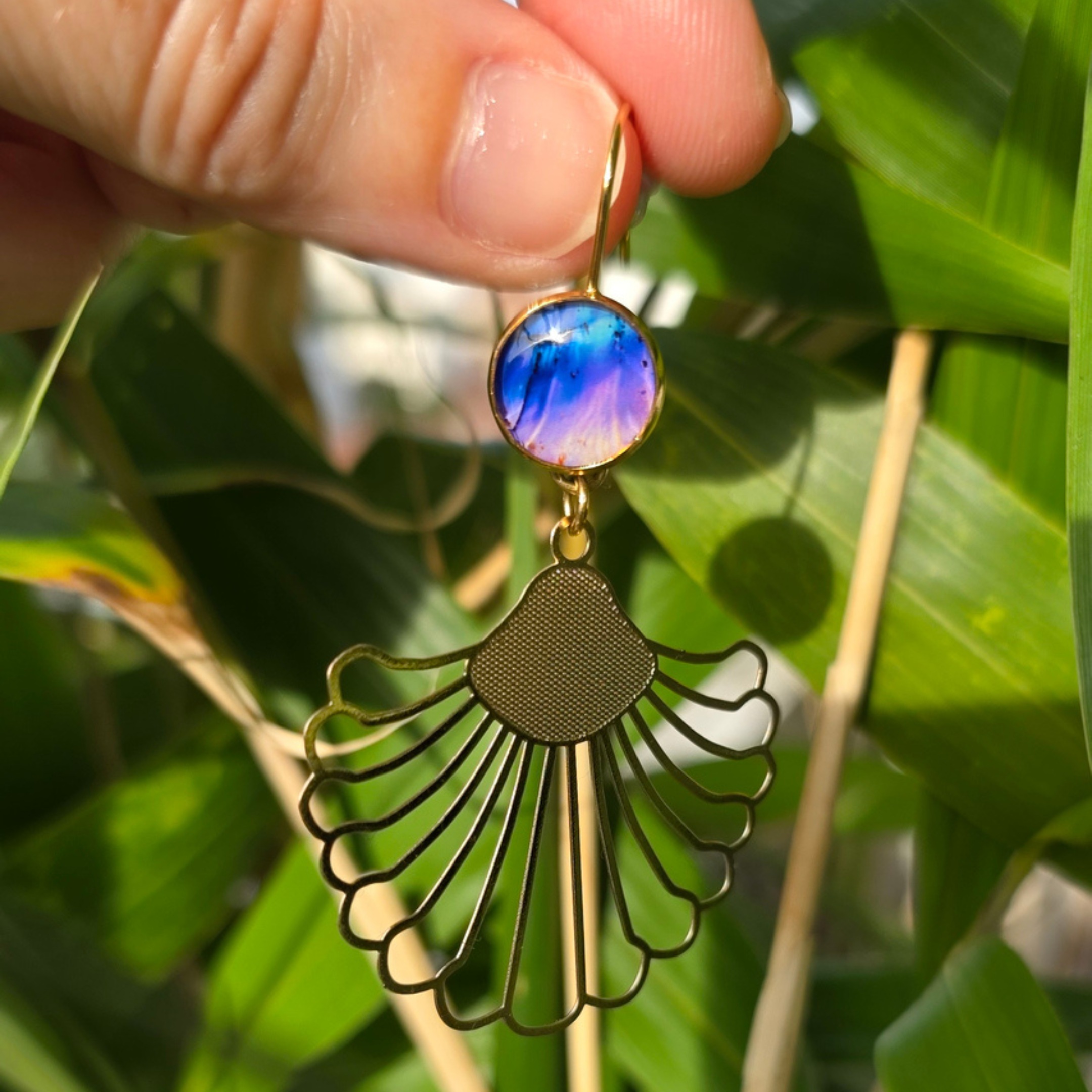 Détail des boucles tropicales nacrées, feuille dorée en éventail et cabochon résiné aux tons violet et bleu